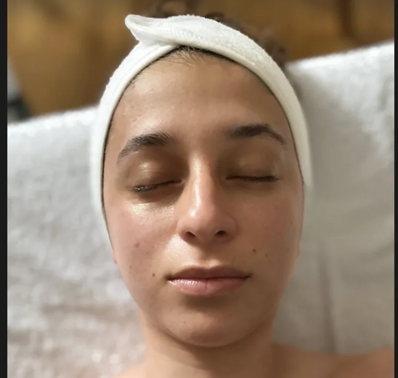 Une cliente aux yeux fermés, un bandeau blanc sur le front, la peau éclatante après le soin
