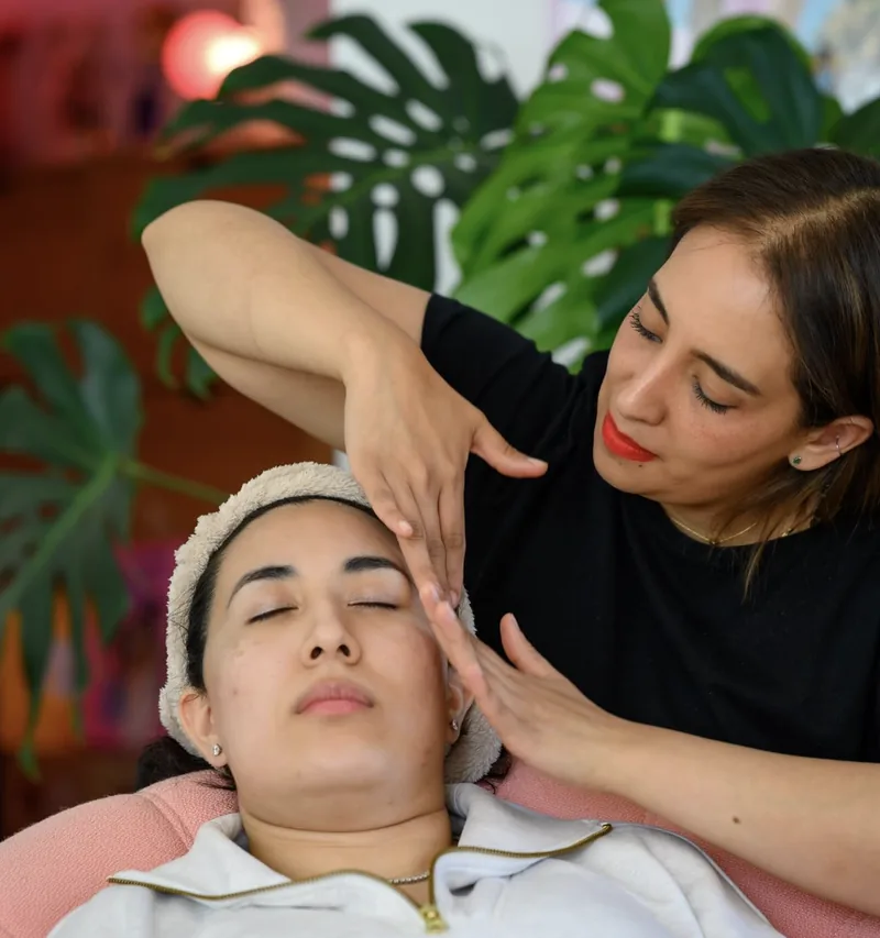 Selene lisse le front d’une cliente aux yeux fermés, le bras levé, entourée de plantes vertes