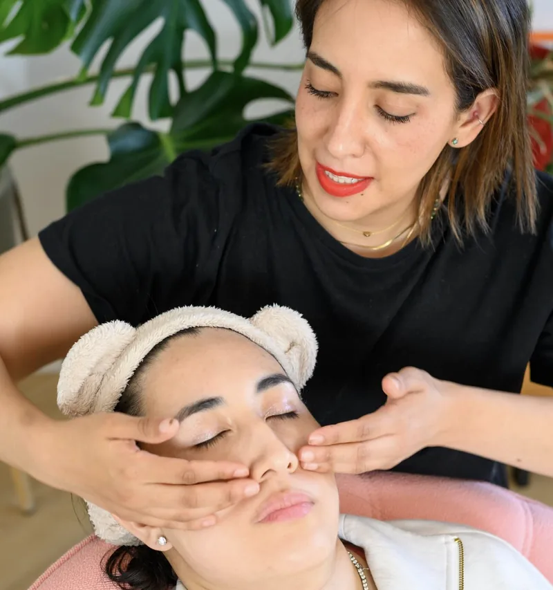 Selene Lopez masse les joues d’une cliente installée dans un fauteuil de velours rose, pendant un soin Kobido