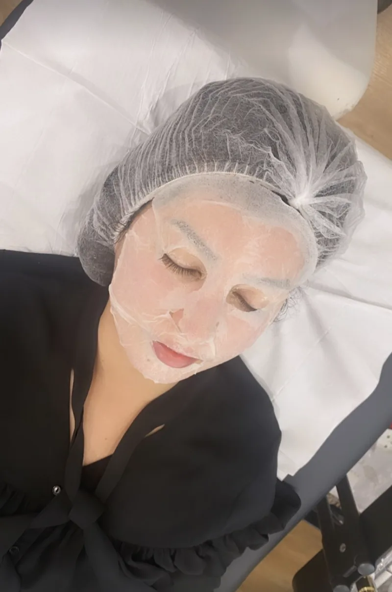 Une cliente allongée, un masque en tissu posé sur le visage, pendant un soin du visage