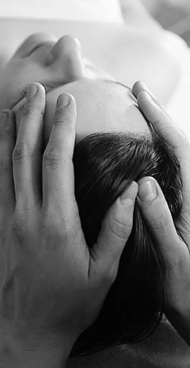 En noir et blanc, des mains qui massent le cuir chevelu d’une personne allongée