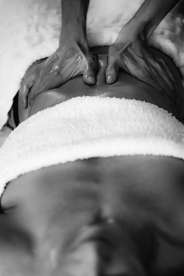 En noir et blanc, des mains qui massent le haut du dos d’une personne allongée sur une serviette