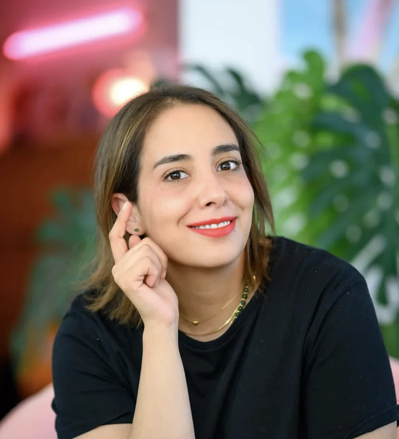 Portrait de Selene Lopez, facialiste, souriante, en tee-shirt noir devant des plantes vertes