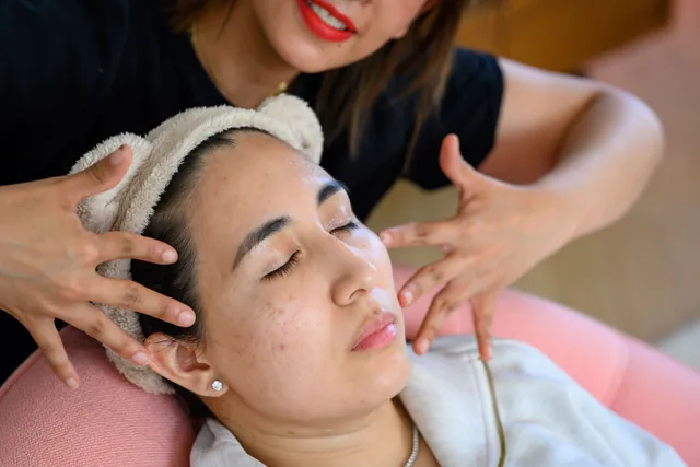 Gros plan des mains de Selene qui massent le visage d’une cliente coiffée d’un bandeau
